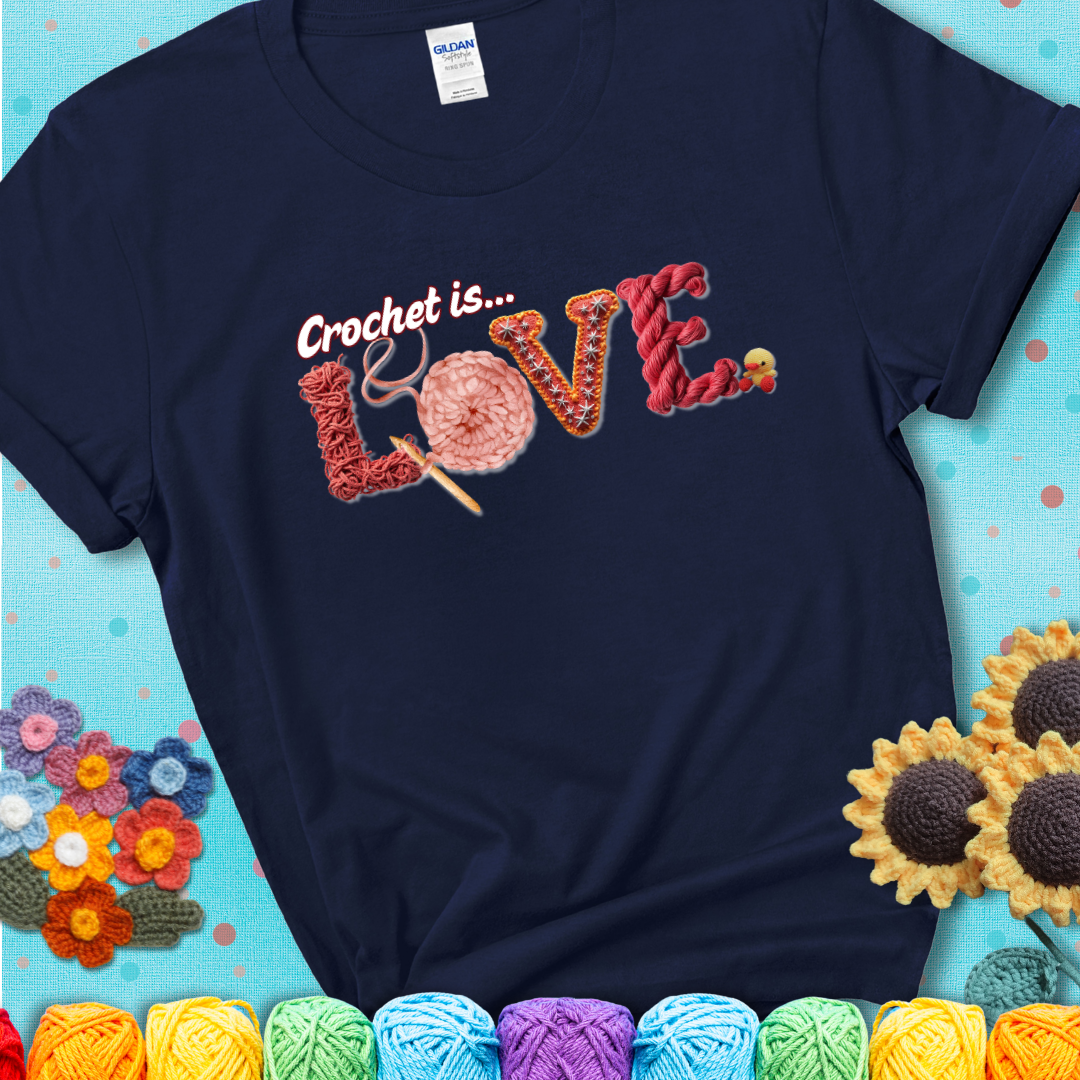 A navy blue t-shirt featuring the word "LOVE" spelled with different crochet textures and yarn in red tones, with the phrase “Crochet is…” above in script.