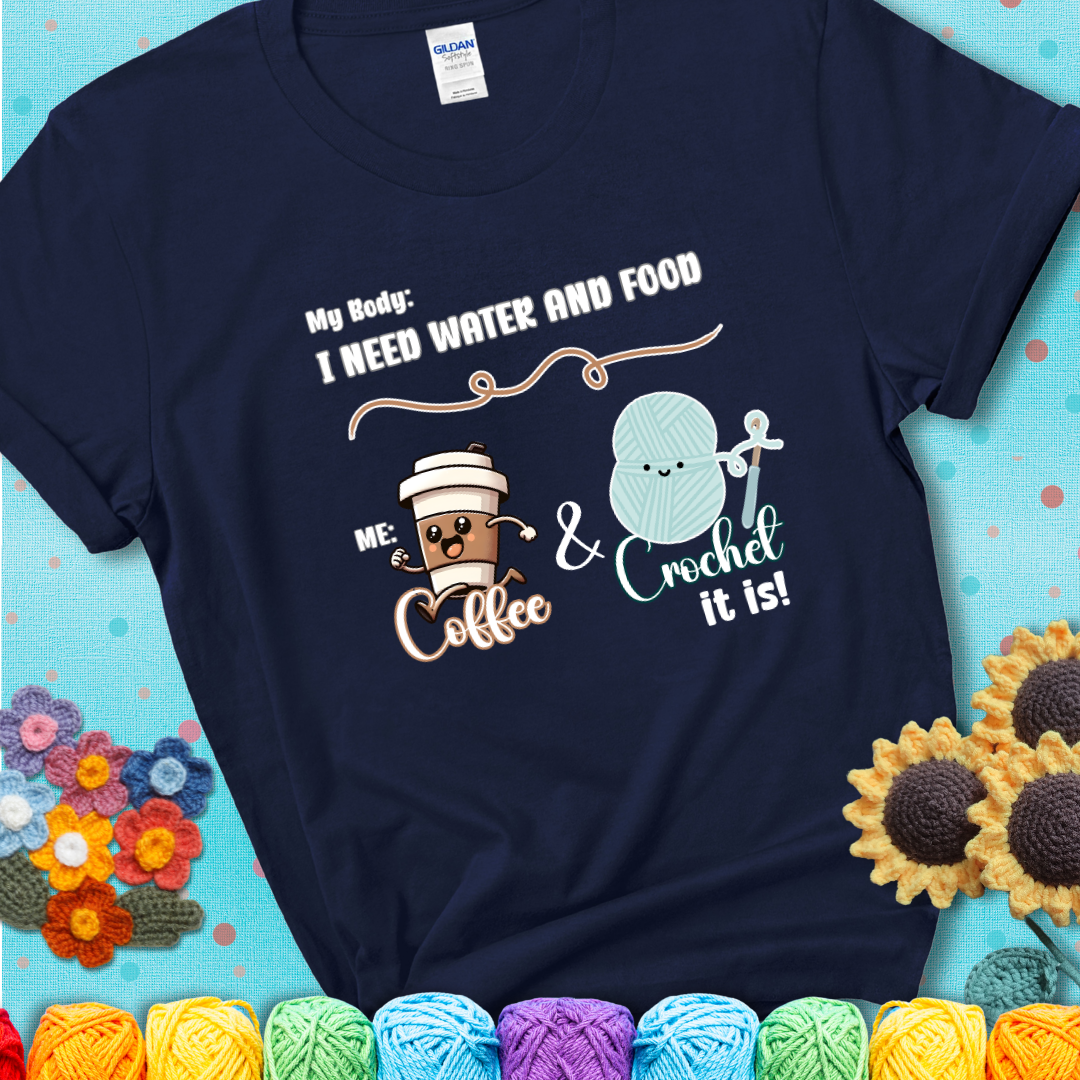 Design reads “My body: I need water and food. Me: Coffee & Crochet it is,” with a smiling coffee cup and yarn ball characters on a navy blue t-shirt.