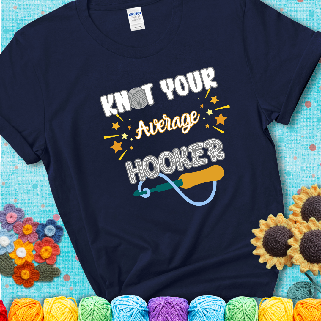 Bold lettering on a navy blue t-shirt with a yarn hook graphic. Text reads: “I'm Not Your Average Hooker.” A cheeky crochet tee for confident crafters who own their skills.