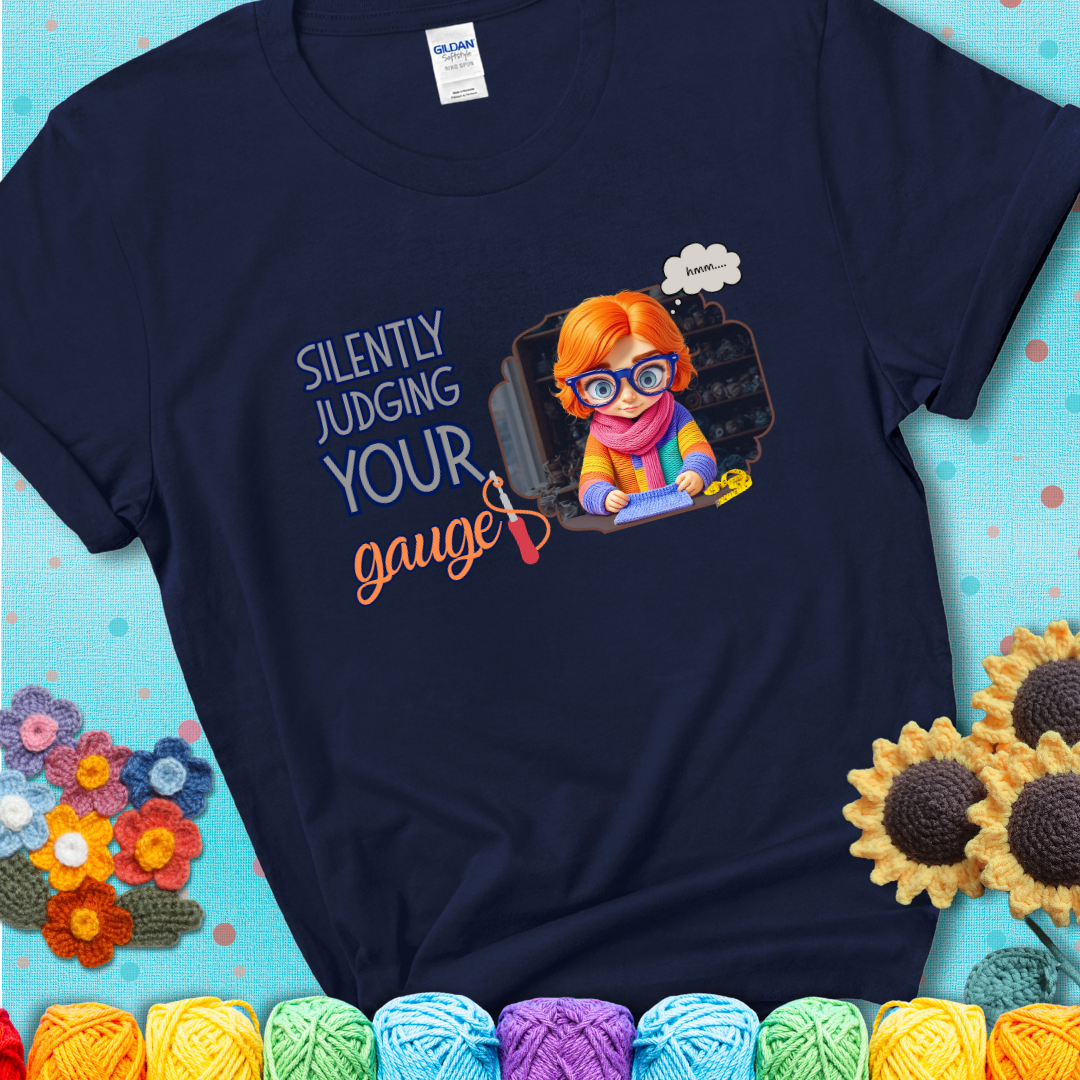 Navy t-shirt with a serious-looking crocheter in rainbow clothing and big glasses, holding a tape measure under the phrase “Silently Judging Your Gauge.”