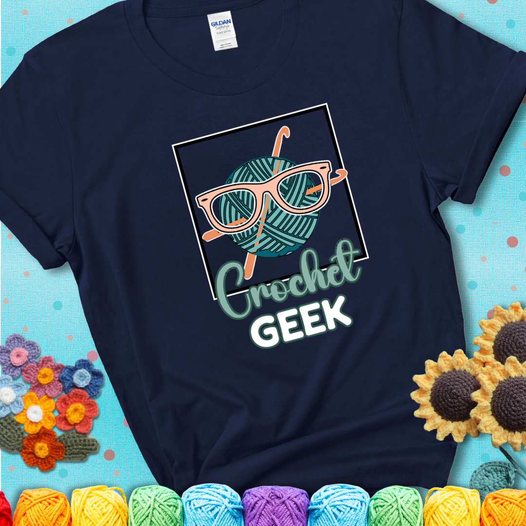 A teal yarn ball with crisscrossed hooks wears oversized nerdy glasses with the phrase “Crochet Geek” in bold, fun text below on a navy blue t-shirt.