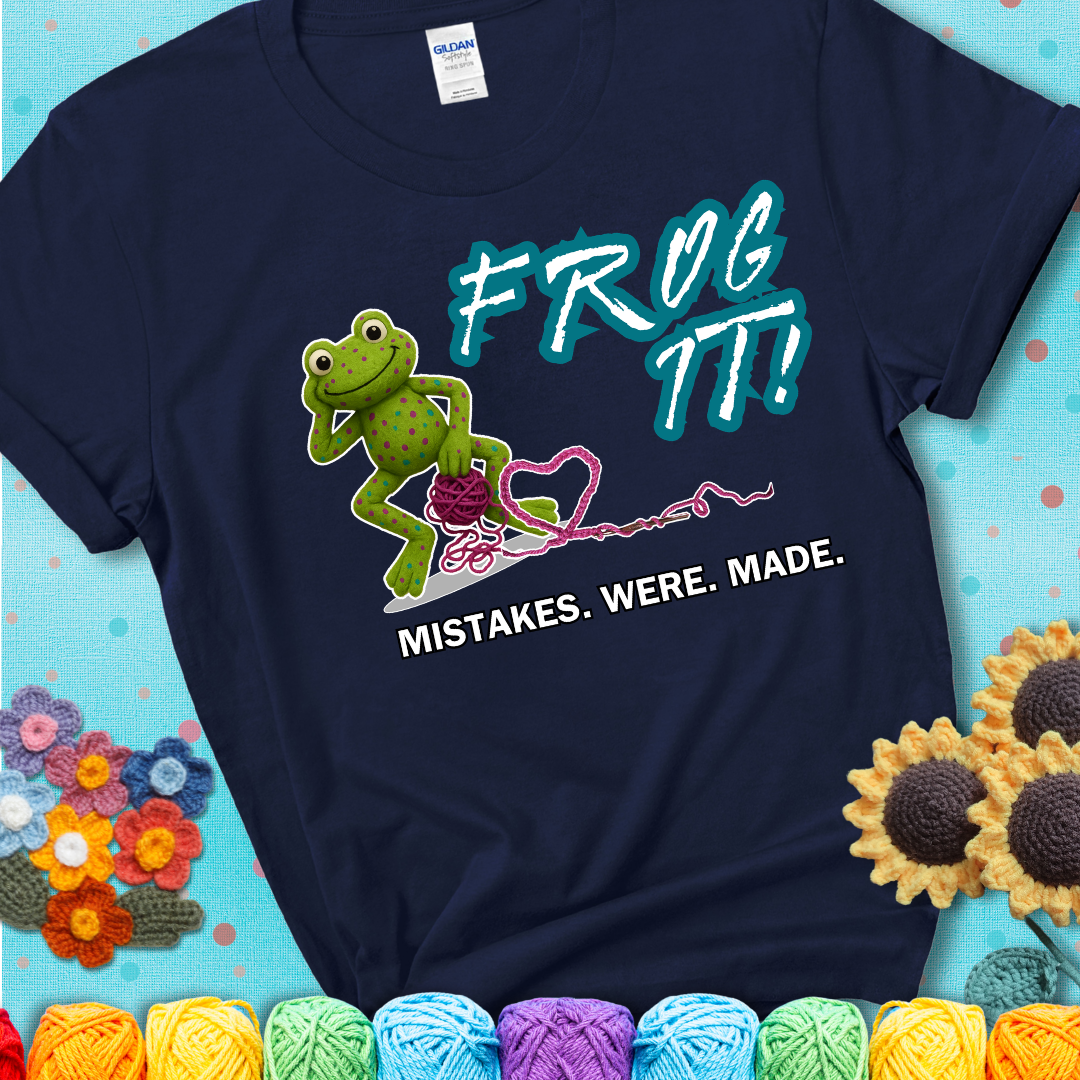 Green frog with yarn and heart-shaped loop. Text reads: “Frog It! Mistakes Were Made.” A playful crochet tee for anyone who's ever had to rip it back, showing a navy blue tee with a teal sunflower background