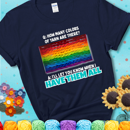 Navy blue t-shirt with rainbow skeins of yarn stacked in color gradient with playful question: “How many colors of yarn are there?” Answer: “I'll let you know when I have them all.”