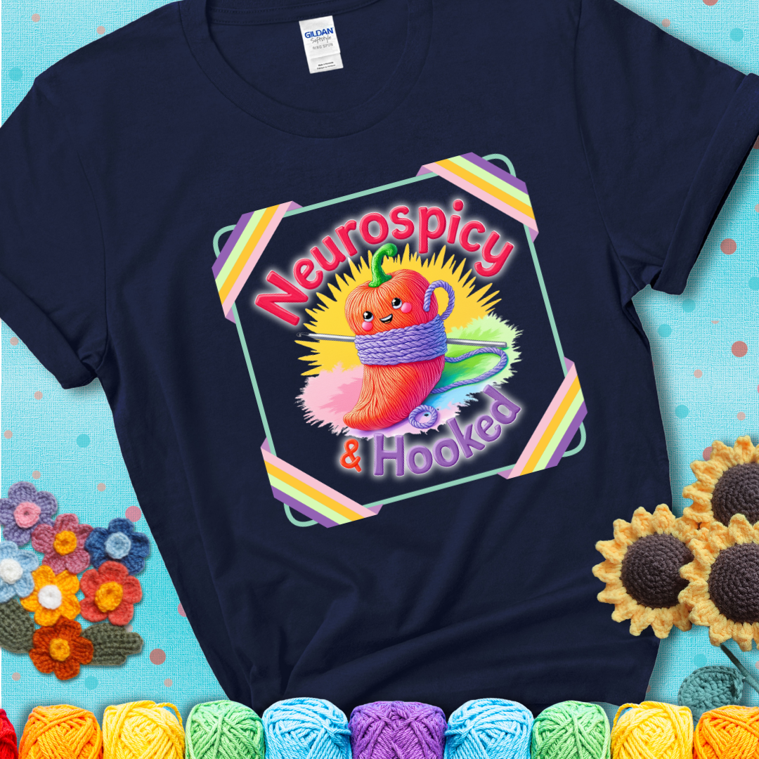 Navy blue t-shirt featuring a smiling red chili pepper wrapped in yarn with a crochet hook, text says “Neurospicy & Hooked.”