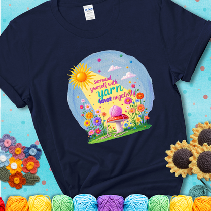 Navy t-shirt featuring a happy spring garden scene with a sunbeam, flowers, and a pink yarn ball on a mushroom, with the quote "Surround yourself with yarn, knot negativity."