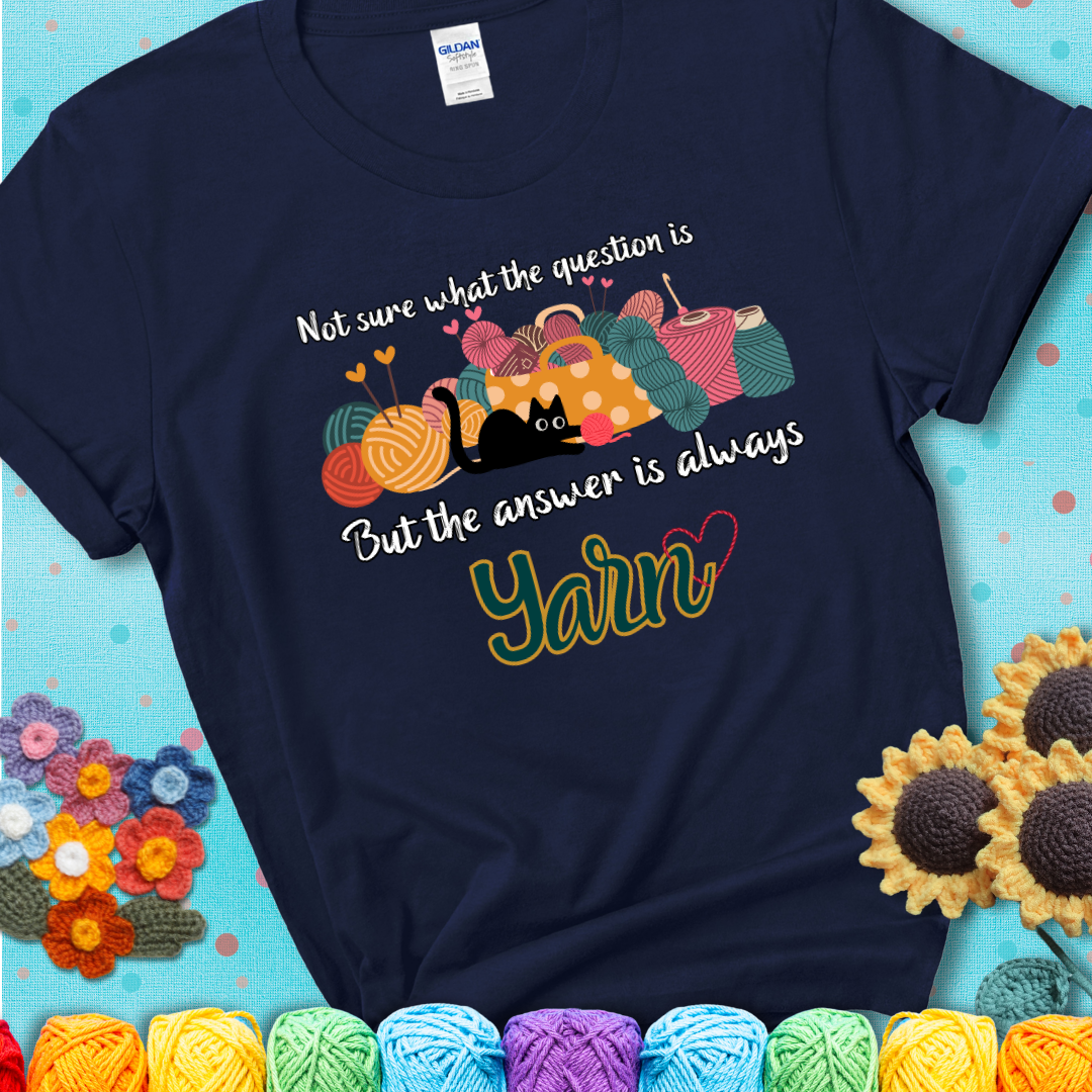 Navy blue t-shirt with a black cat beside a basket of colorful yarn and the phrase, “Not Sure What The Question Was, But The Answer Is Yarn.”