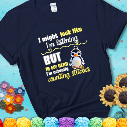 Navy blue t-shirt shows a crocheted penguin next to the text “I might look like I’m listening but in my head I’m actually counting stitches.”