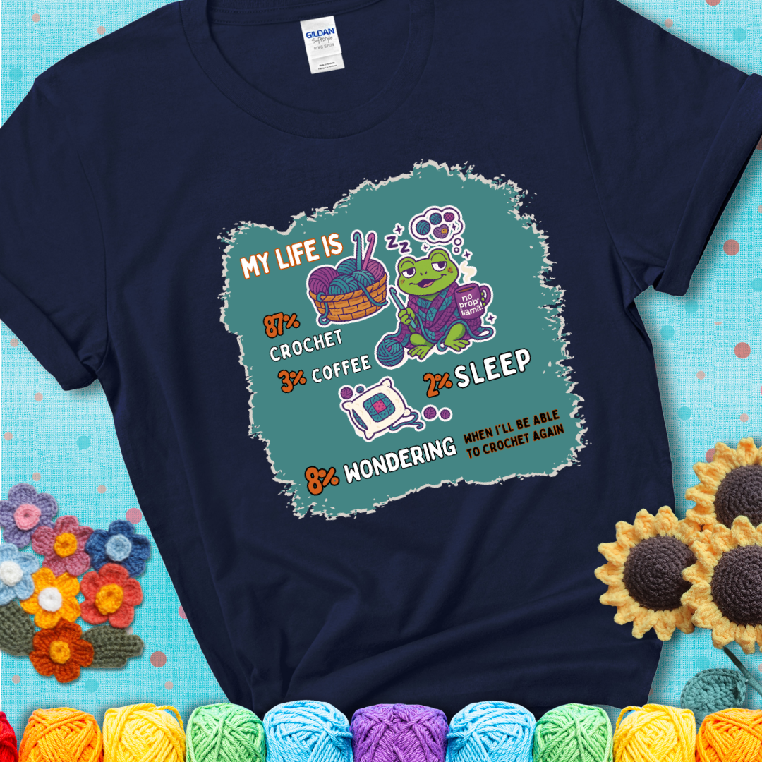Navy blue t-shirt with a crocheting frog, coffee, yarn, and text showing a playful life breakdown: 87% crochet, 3% coffee, 2% sleep, 8% wondering when to crochet again.