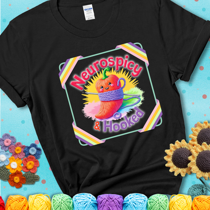 Black t-shirt featuring a smiling red chili pepper wrapped in yarn with a crochet hook, text says “Neurospicy & Hooked.”