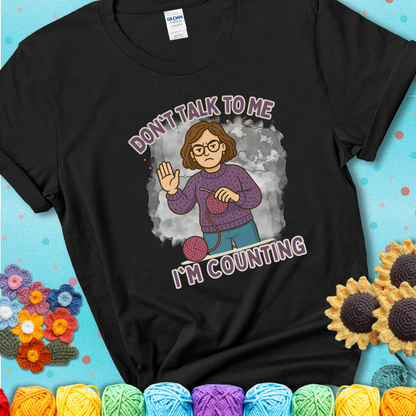 Black t-shirt with an annoyed maker holding up a hand beside yarn, with the phrase “Don’t Talk To Me, I’m Counting.”