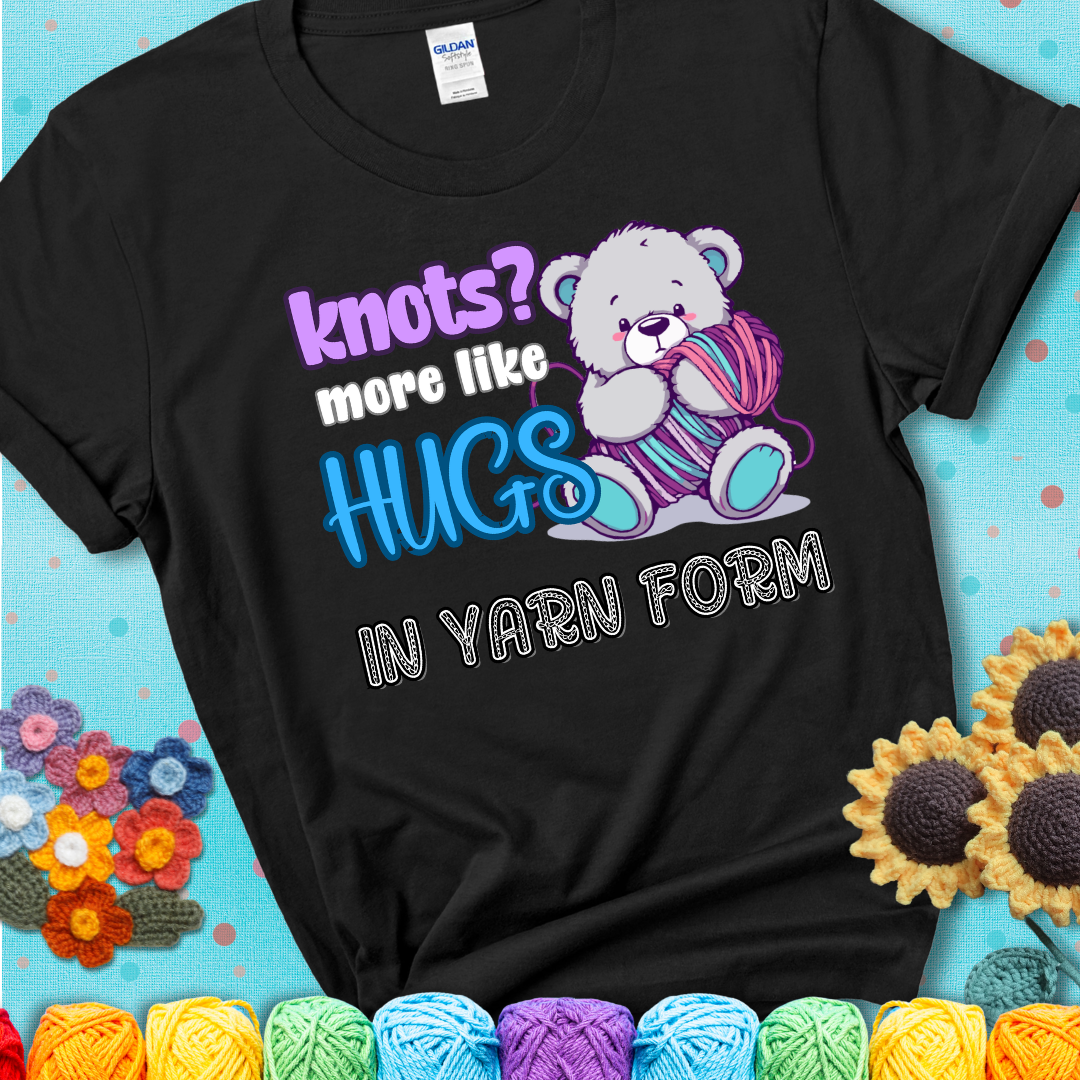 Cute teddy bear holding colorful yarn ball with hearts. Text reads: “Knots? More Like Hugs in Yarn Form.” Perfect for cozy gift-givers and yarn lovers, showing a black tee with a teal sunflower background
