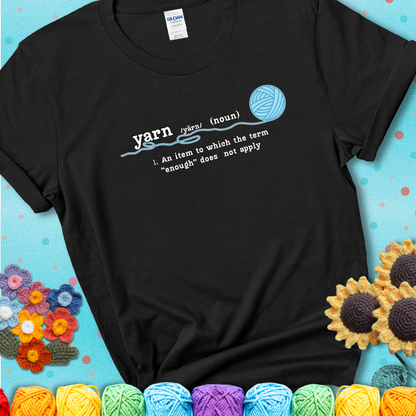 Black t-shirt with a definition-style yarn graphic reading “An item to which the word ‘enough’ does not apply,” plus a blue ball of yarn with a loose strand.