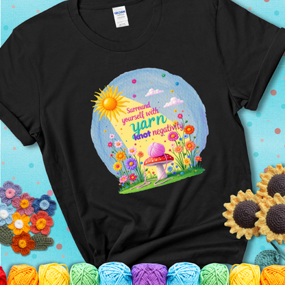 Black  t-shirt featuring a happy spring garden scene with a sunbeam, flowers, and a pink yarn ball on a mushroom, with the quote "Surround yourself with yarn, knot negativity."