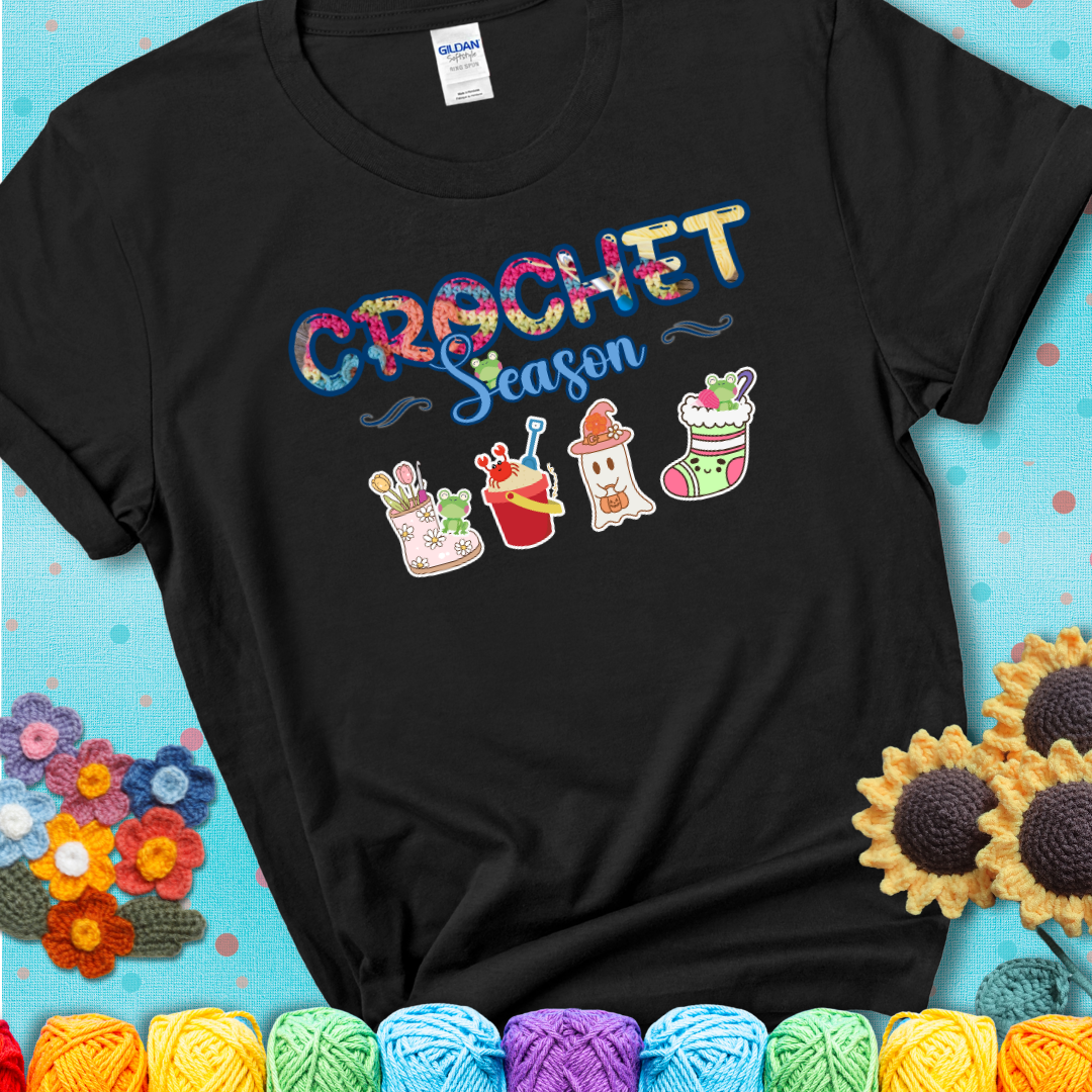 Black t-shirt shows the words “Crochet Season” with cute seasonal icons below: a spring boot with hooks, summer bucket with crab, fall ghost with pumpkin hat, winter stocking, and tiny frogs.
