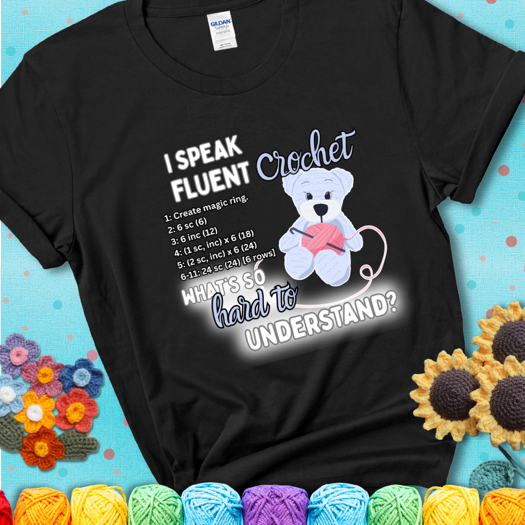 A cute crochet bear holding a yarn ball, surrounded by a short crochet pattern. The phrase reads “I Speak Fluent Crochet – What’s so hard to understand?” on a black  t-shirt.