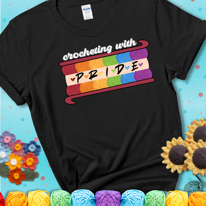 Yarn skeins in rainbow colors stacked in a hook shape. Text reads “Crocheting With Pride” showing a black tee with a teal sunflower background