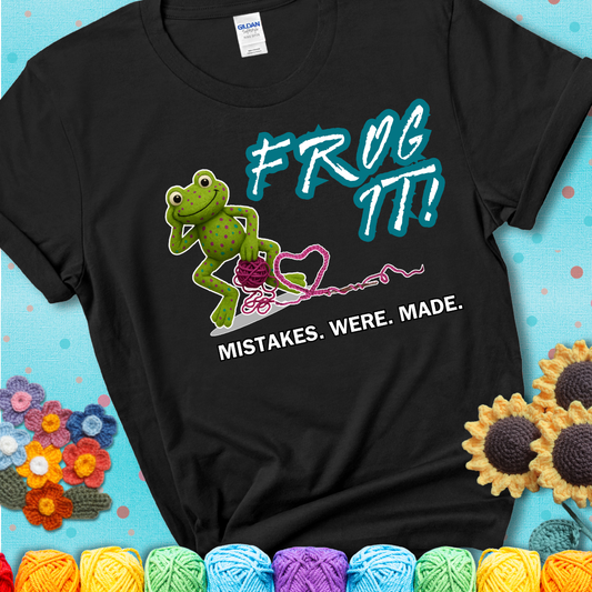 Green frog with yarn and heart-shaped loop. Text reads: “Frog It! Mistakes Were Made.” A playful crochet tee for anyone who's ever had to rip it back, showing a black tee with a teal sunflower background