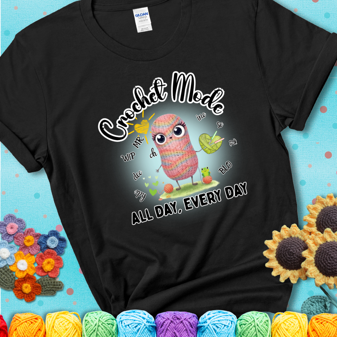 Black t-shirt with a kawaii-style rainbow yarn character surrounded by crochet stitch abbreviations and holding a yarn heart, with text “Crochet Mode All Day, Every Day.”