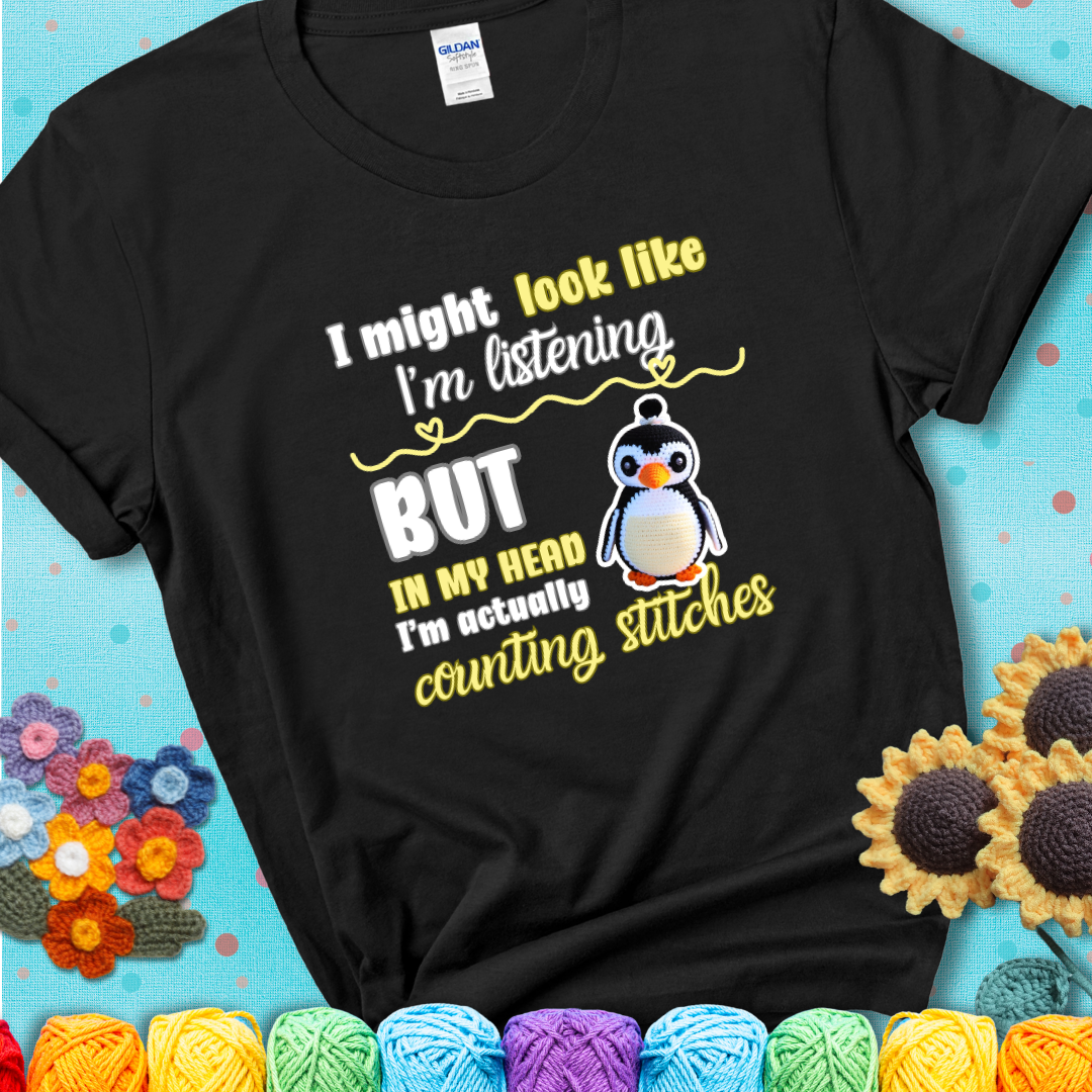 Black t-shirt shows a crocheted penguin next to the text “I might look like I’m listening but in my head I’m actually counting stitches.”