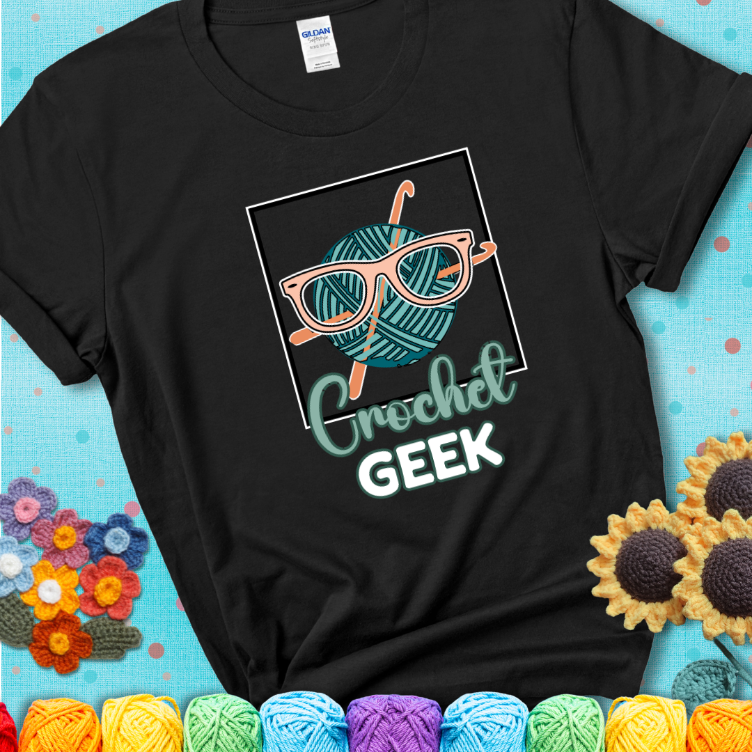 A teal yarn ball with crisscrossed hooks wears oversized nerdy glasses with the phrase “Crochet Geek” in bold, fun text below on a black t-shirt.