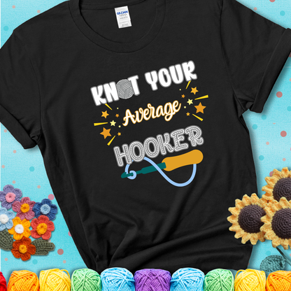 Bold lettering on a black t-shirt with a yarn hook graphic. Text reads: “I'm Not Your Average Hooker.” A cheeky crochet tee for confident crafters who own their skills.