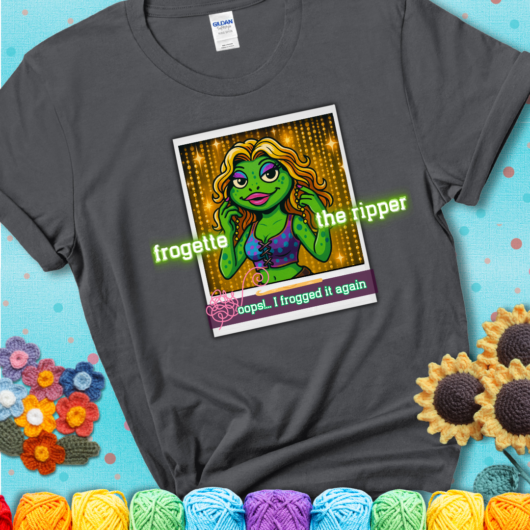 Retro-styled illustration of a glamorous green frog in a sparkly outfit, labeled "Frogette the Ripper" with the phrase “Oops! I frogged it again” below, referencing both crochet and pop culture showing a charcoal grey tee with a teal sunflower background