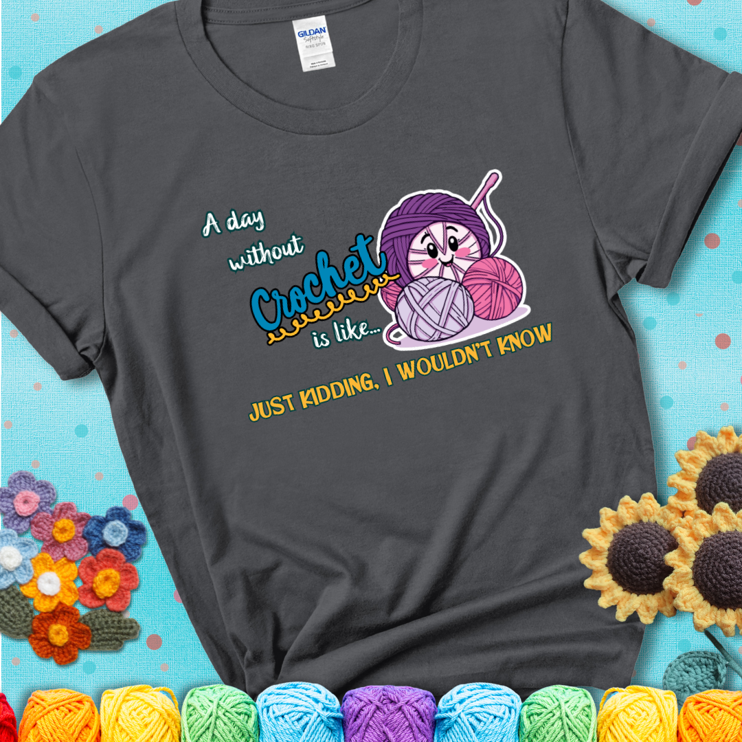 Charcoal grey t-shirt showing a smiling yarn ball character with text “A day without crochet is like... just kidding, I wouldn’t know”; funny crochet t-shirt.