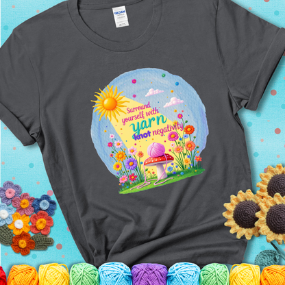 Charcoal grey t-shirt featuring a happy spring garden scene with a sunbeam, flowers, and a pink yarn ball on a mushroom, with the quote "Surround yourself with yarn, knot negativity."
