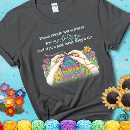 Charcoal t-shirt with an illustration of two hands crocheting a rainbow swatch, surrounded by colorful flowers and the phrase “These hands were made for crocheting… and that’s just what they’ll do.”