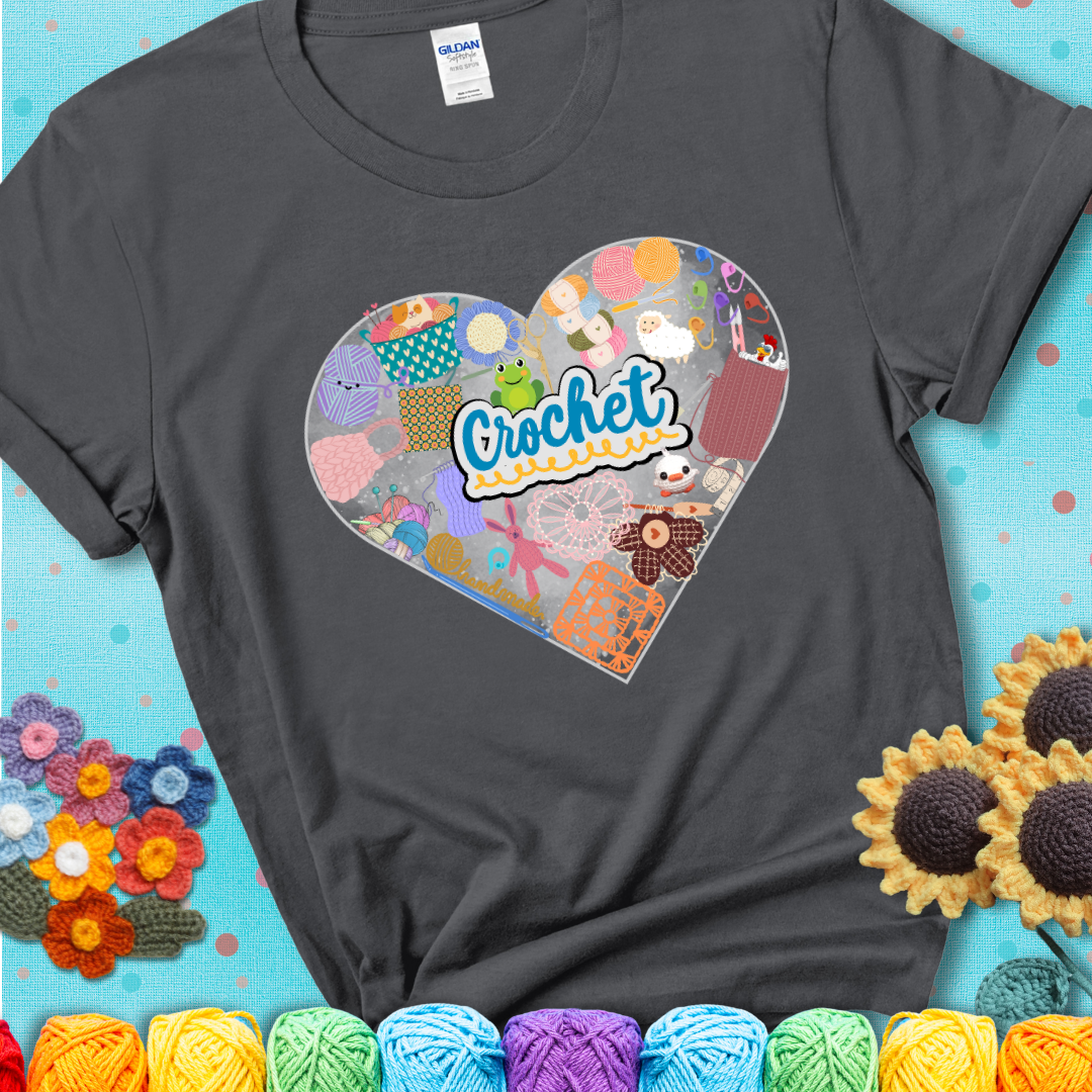A heart filled with colorful crochet essentials including yarn, hooks, scissors, notions, and handmade items, with the word "Crochet" prominently in the center of a charcoal grey t-shirt.