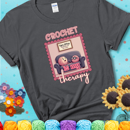 Charcoal grey t-shirt showing a simple text design with yarn cartoon figures. Text reads: “Crochet is My Therapy.” A calming tee for fiber lovers who find healing in every stitch.