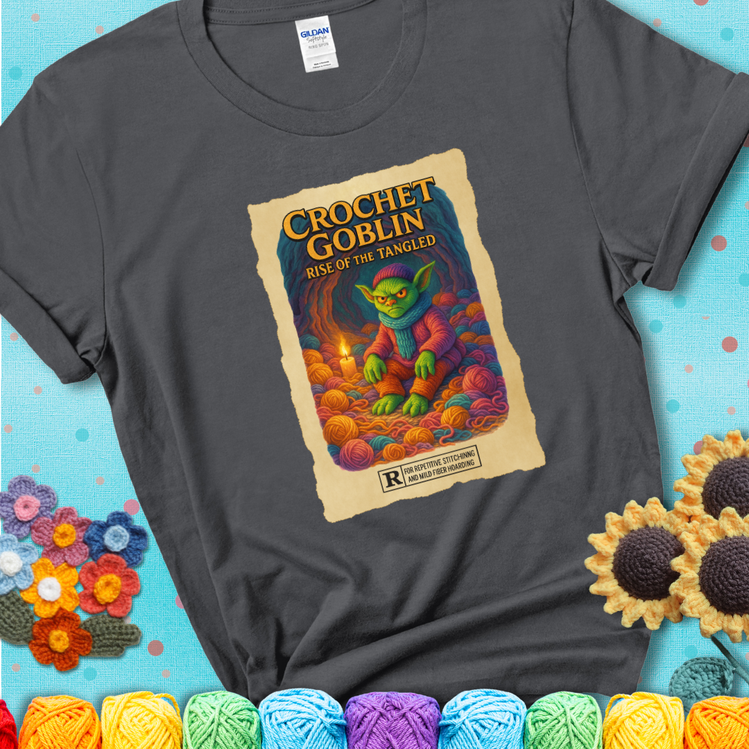 Crochet goblin surrounded by chaotic yarn stash in a cave-like lair. Text reads: “Crochet Goblin: Rise of the Tangled.” A funny fantasy-style charcoal grey tee for yarn hoarders and goblin-mode crafters.