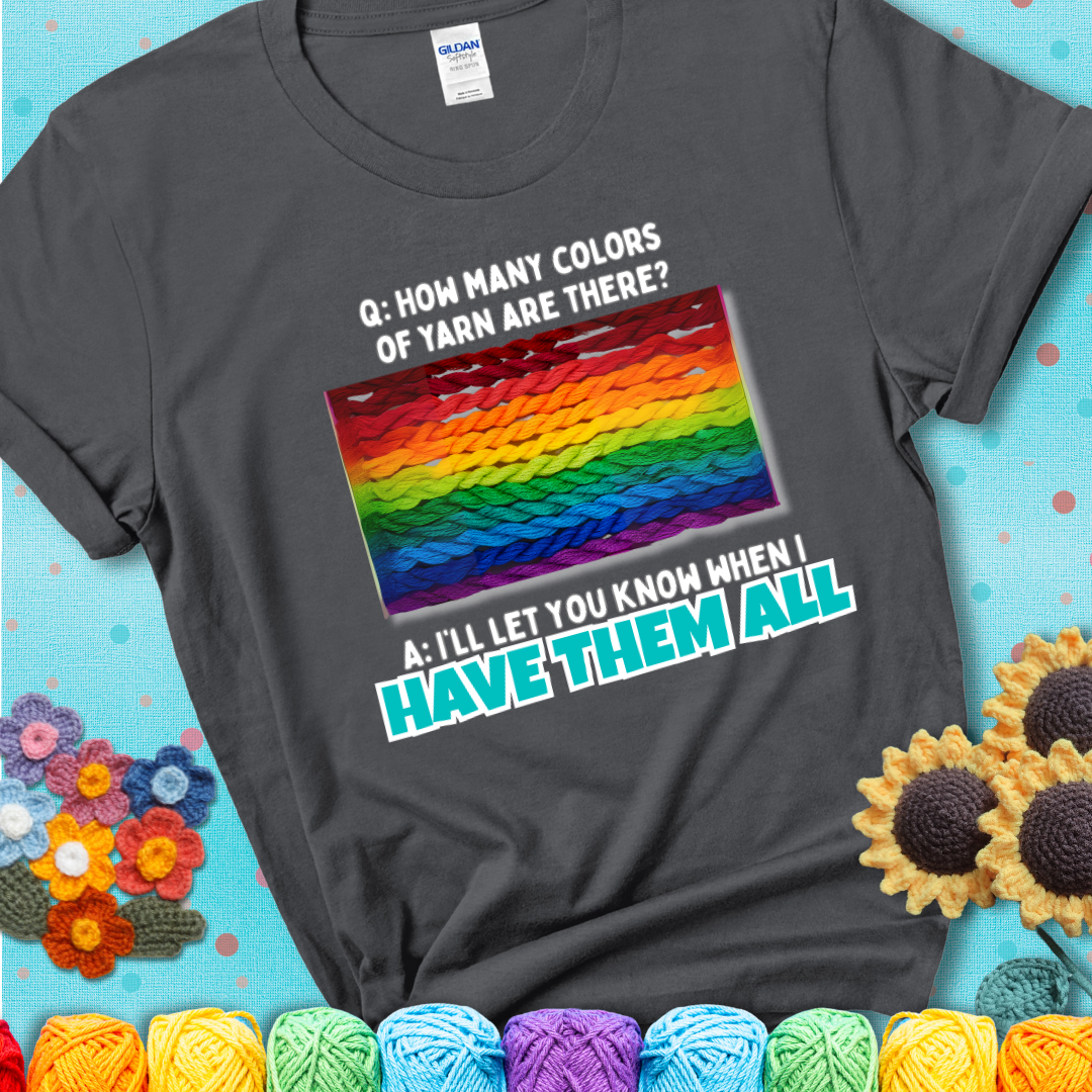 Charcoal grey t-shirt with rainbow skeins of yarn stacked in color gradient with playful question: “How many colors of yarn are there?” Answer: “I'll let you know when I have them all.”