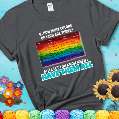 Charcoal grey t-shirt with rainbow skeins of yarn stacked in color gradient with playful question: “How many colors of yarn are there?” Answer: “I'll let you know when I have them all.”