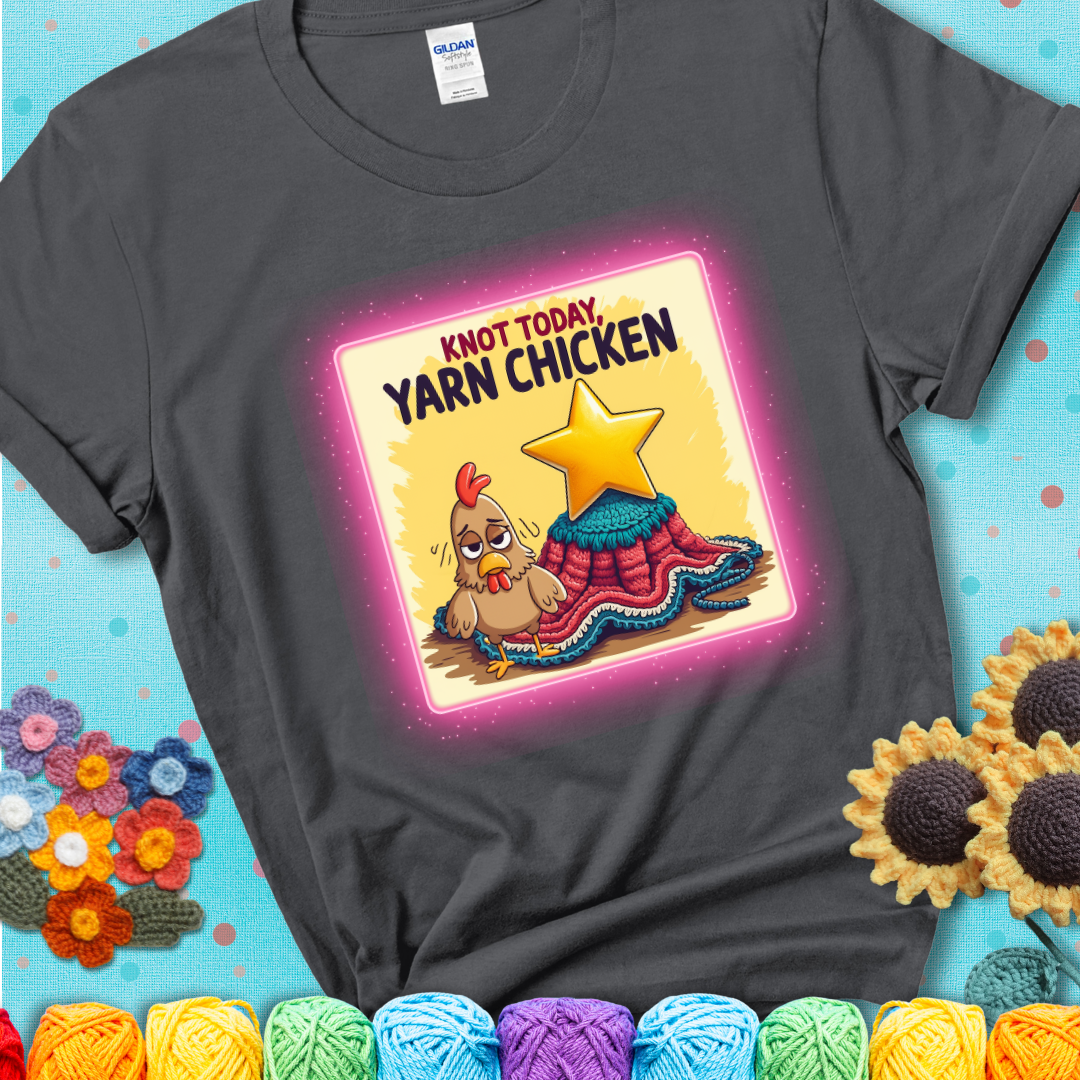 A charcoal grey t-shirt showing a frazzled cartoon chicken stands next to a nearly-finished project with minimal yarn left, with the phrase “Knot Today, Yarn Chicken” above.