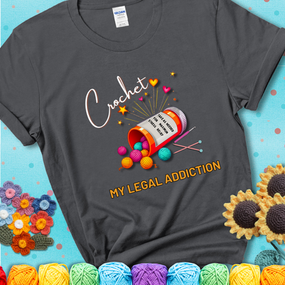 Charcoal t-shirt with a prescription bottle spilling colorful yarn balls, small crochet details, and the phrase “Crochet: My Legal Addiction.”