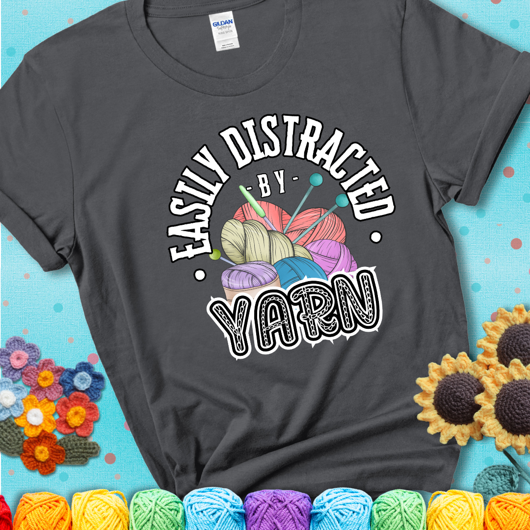 If yarn steals your focus every Design reads 'Easily Distracted By Yarn', perfect crochet gift for yarn lovers; showing a charcoal grey tee with a teal sunflower background