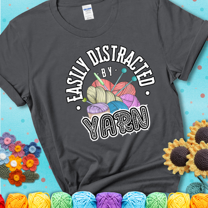 If yarn steals your focus every Design reads 'Easily Distracted By Yarn', perfect crochet gift for yarn lovers; showing a charcoal grey tee with a teal sunflower background