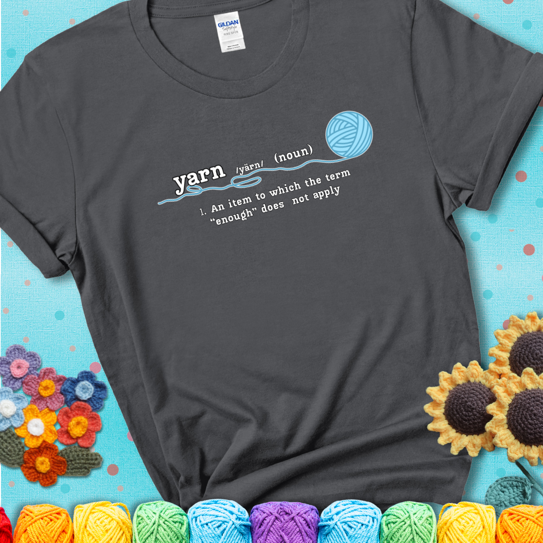 Charcoal t-shirt with a definition-style yarn graphic reading “An item to which the word ‘enough’ does not apply,” plus a blue ball of yarn with a loose strand.