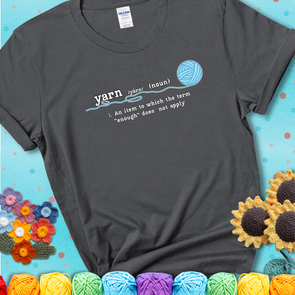 Charcoal t-shirt with a definition-style yarn graphic reading “An item to which the word ‘enough’ does not apply,” plus a blue ball of yarn with a loose strand.