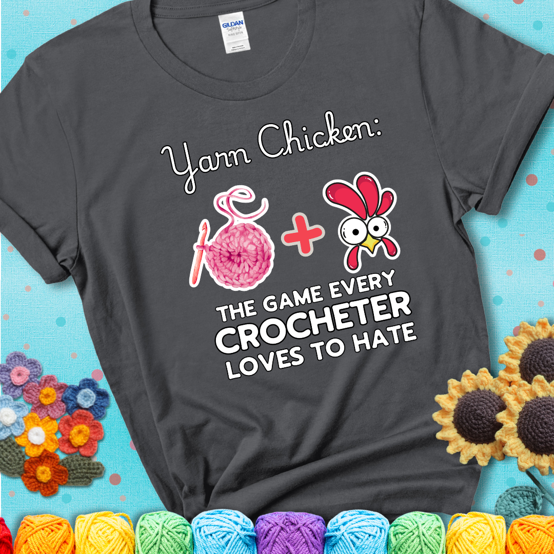 Cartoon chicken inside a yarn ball with crochet circle background. Text reads: “Yarn Chicken: The Game Every Crocheter Loves to Lose.” A fun and relatable tee for fiber artists who like to live on the edge, showing a charcoal grey tee with a teal sunflower background