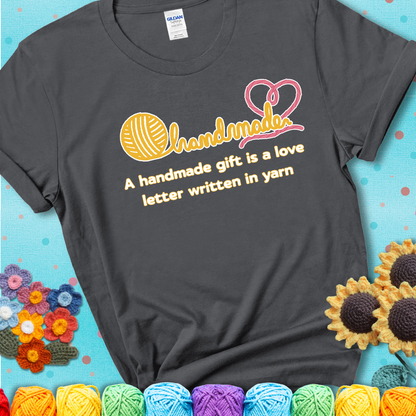 Soft script-style design with heart detail. Text reads: “A Handmade Gift Is a Love Letter Written in Yarn.” A sweet and sentimental shirt for crocheters who craft from the heart, showing a charcoal grey tee with a teal sunflower background