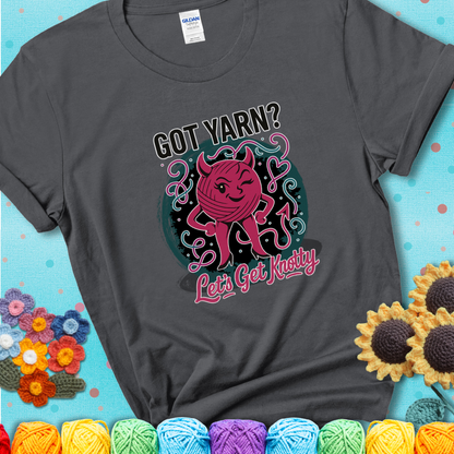 Charcoal t-shirt with a cheeky pink yarn ball wearing devil horns, arms, and legs, winking beneath the phrase “Got Yarn? Let’s Get Knotty