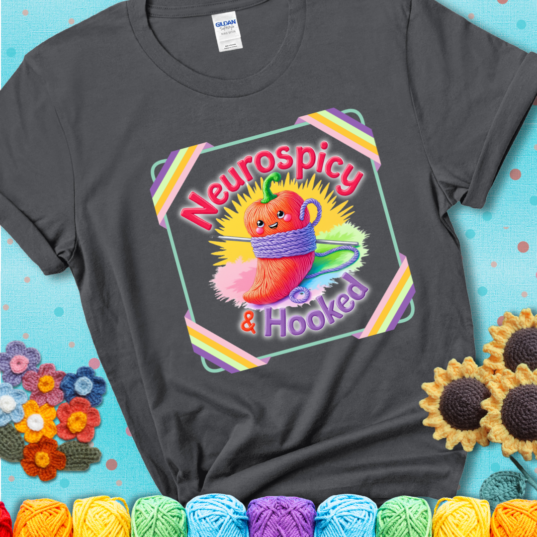 Charcoal grey t-shirt featuring a smiling red chili pepper wrapped in yarn with a crochet hook, text says “Neurospicy & Hooked.”