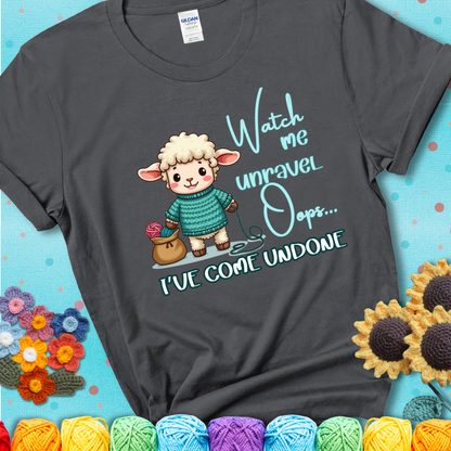 Charcoal grey t-shirt with a cute sheep holding yarn looks startled with the phrase “Watch me unravel… Oops, I’ve come undone.” Perfect mix of whimsy and yarn life chaos.