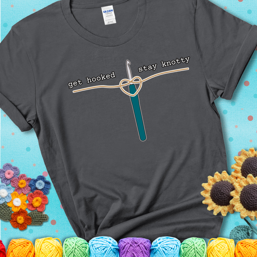 Hooked on yarn? Same Design reads 'Get Hooked, Stay Knotty' , perfect crochet gift for yarn lovers, showing a charcoal grey tee with a teal sunflower background