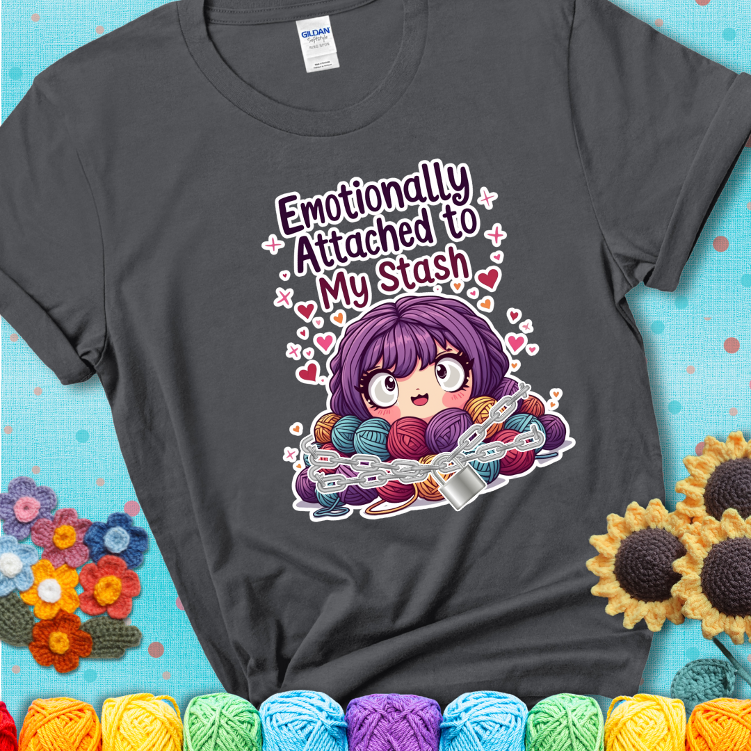 Adorable character with wide eyes hugging a yarn stash wrapped in chains and a lock, with the text “Emotionally Attached to My Stash”  on a charcoal grey tee.