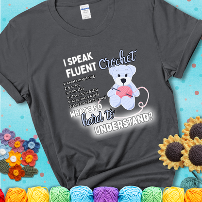 A cute crochet bear holding a yarn ball, surrounded by a short crochet pattern. The phrase reads “I Speak Fluent Crochet – What’s so hard to understand?” on a charcoal grey t-shirt.