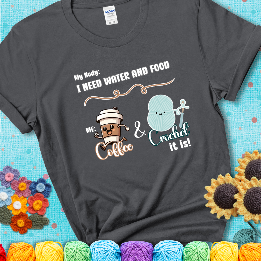 Design reads “My body: I need water and food. Me: Coffee & Crochet it is,” with a smiling coffee cup and yarn ball characters on a charcoal grey t-shirt.