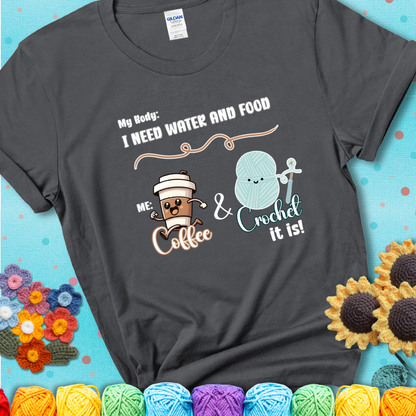 Design reads “My body: I need water and food. Me: Coffee & Crochet it is,” with a smiling coffee cup and yarn ball characters on a charcoal grey t-shirt.